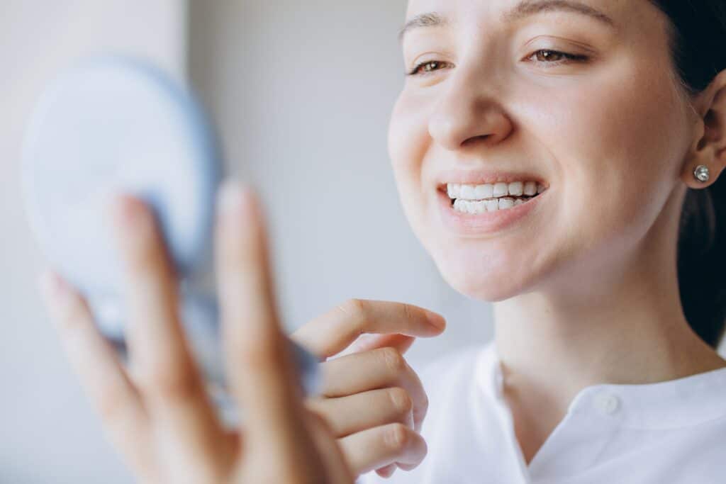 young woman checking teeth in mirror, Teeth Whitening