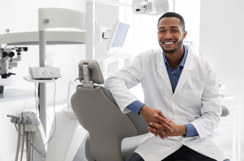 A male dentist smiling while sitting in his office
