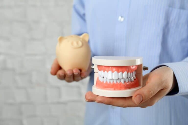 Person holding a piggy bank in one hand and a set of dentures in the other, symbolizing denture affordability and budgeting.