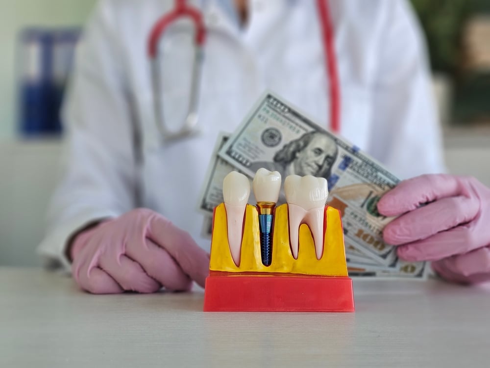 A dentist showing a dental implant model and holding cash
