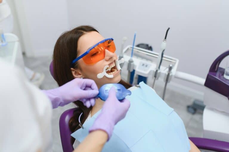 Patient receiving professional in-office teeth whitening with a blue LED light.