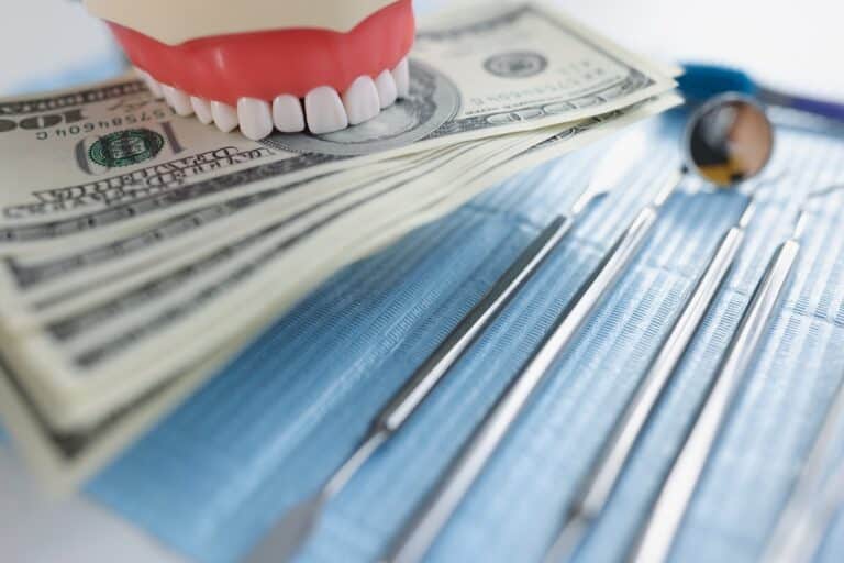 Model teeth next to a stack of dollars next to dentist tools