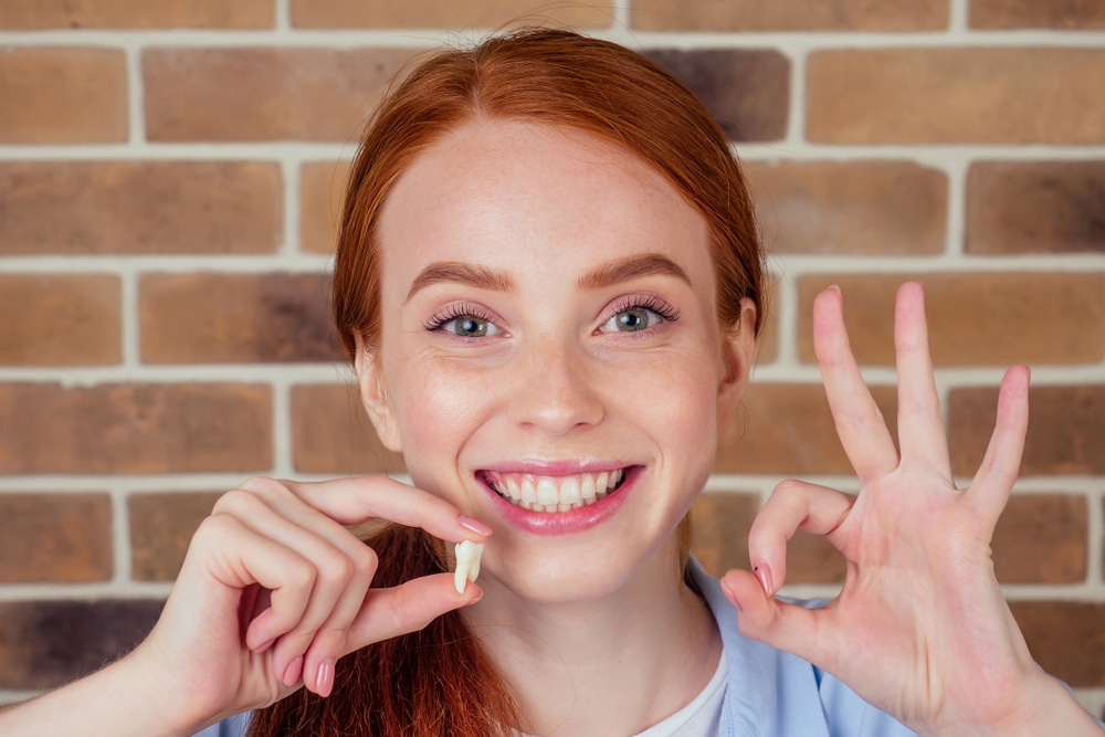 A smiling young girl holding an extracted tooth
