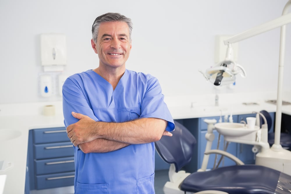 What is Conscious Sedation Dentistry? 3 A smiling male dentist standing in his office with his arms crossed